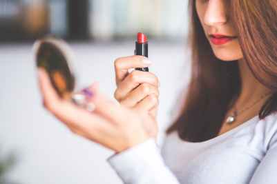 woman with brown hair doing lipstick and holding little mirror